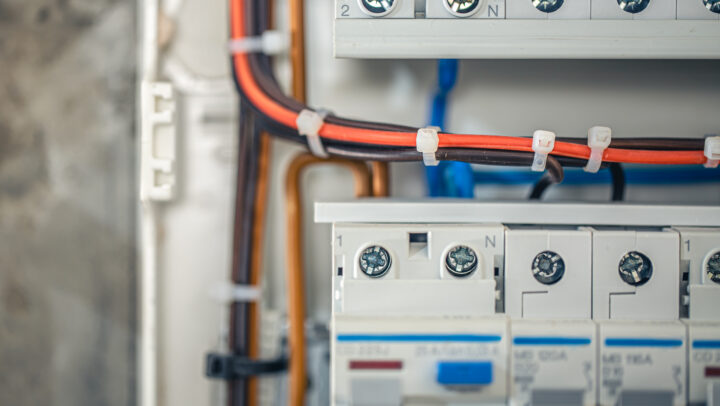 Close-up of an electrical breaker panel with red and black wires tied by white zip ties and labeled terminals (N) and numbered positions.