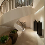 Elegant curved white spiral staircase inside a modern lobby, with metal railings and warm candlelight along the wall.