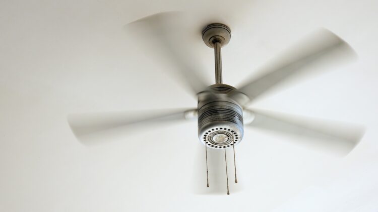 Ceiling fan in motion with blurred blades, mounted to a white ceiling.