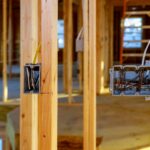 Wood framing with exposed studs and hanging electrical wires in a building under construction, showing junction boxes on the studs, construction site.
