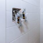 Exposed electrical wiring and two switches protruding from an open wall box in a tiled bathroom.