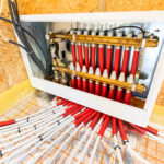 Industrial hydraulic manifold inside an open metal cabinet with brass fittings and many red and white insulated hoses connected to timing valves.